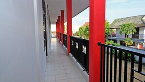Un corredor cubierto con pilares rojos y barandillas negras, que conduce a un edificio con tejado de baldosas.