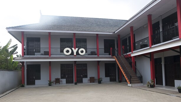 Un edificio de dos pisos con un llamativo letrero 'OYO', varios balcones y una escalera central.