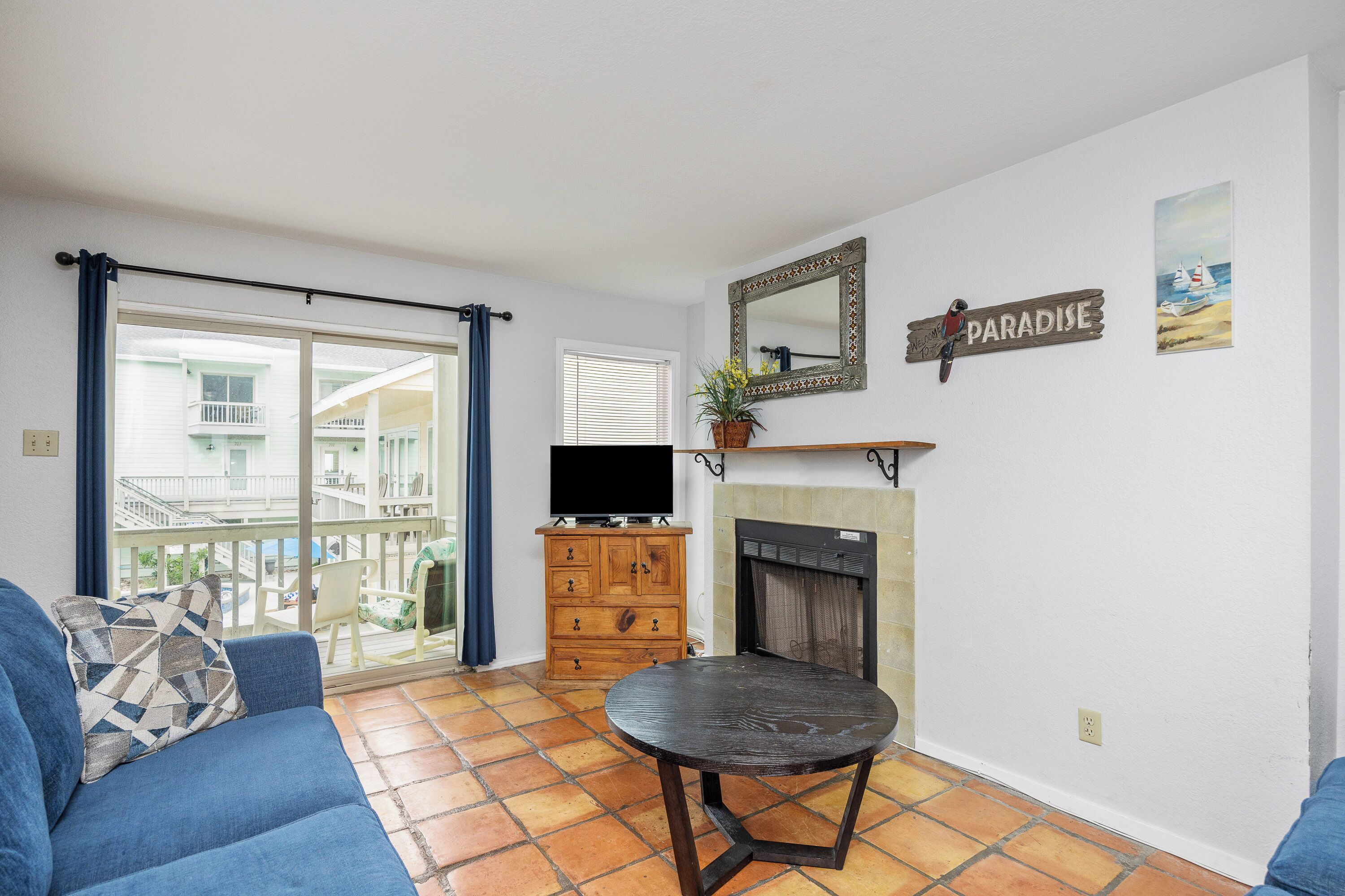 A living room with a fireplace, a television on a wooden cabinet, and a balcony with a view of a building.