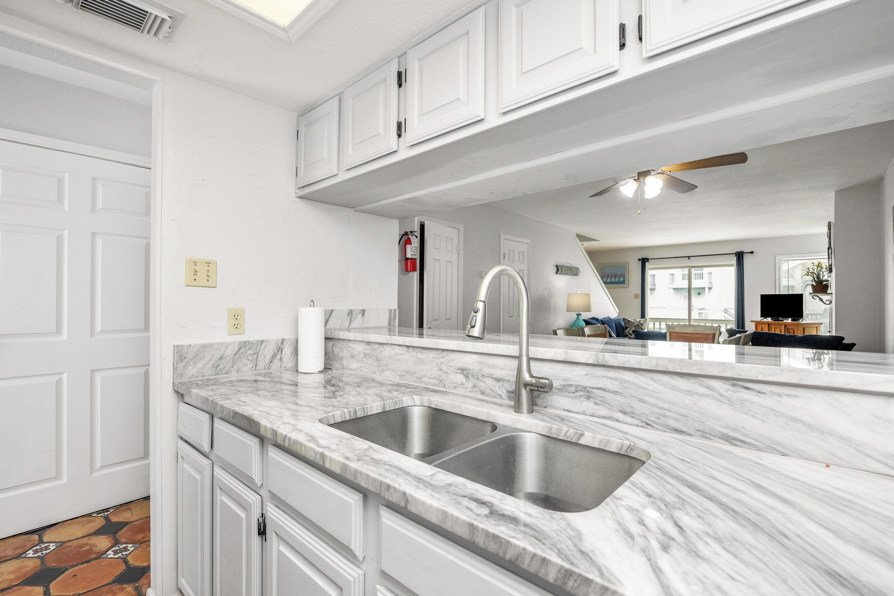 A kitchen with white cabinets, a marble countertop, a stainless steel sink, and a ceiling fan.