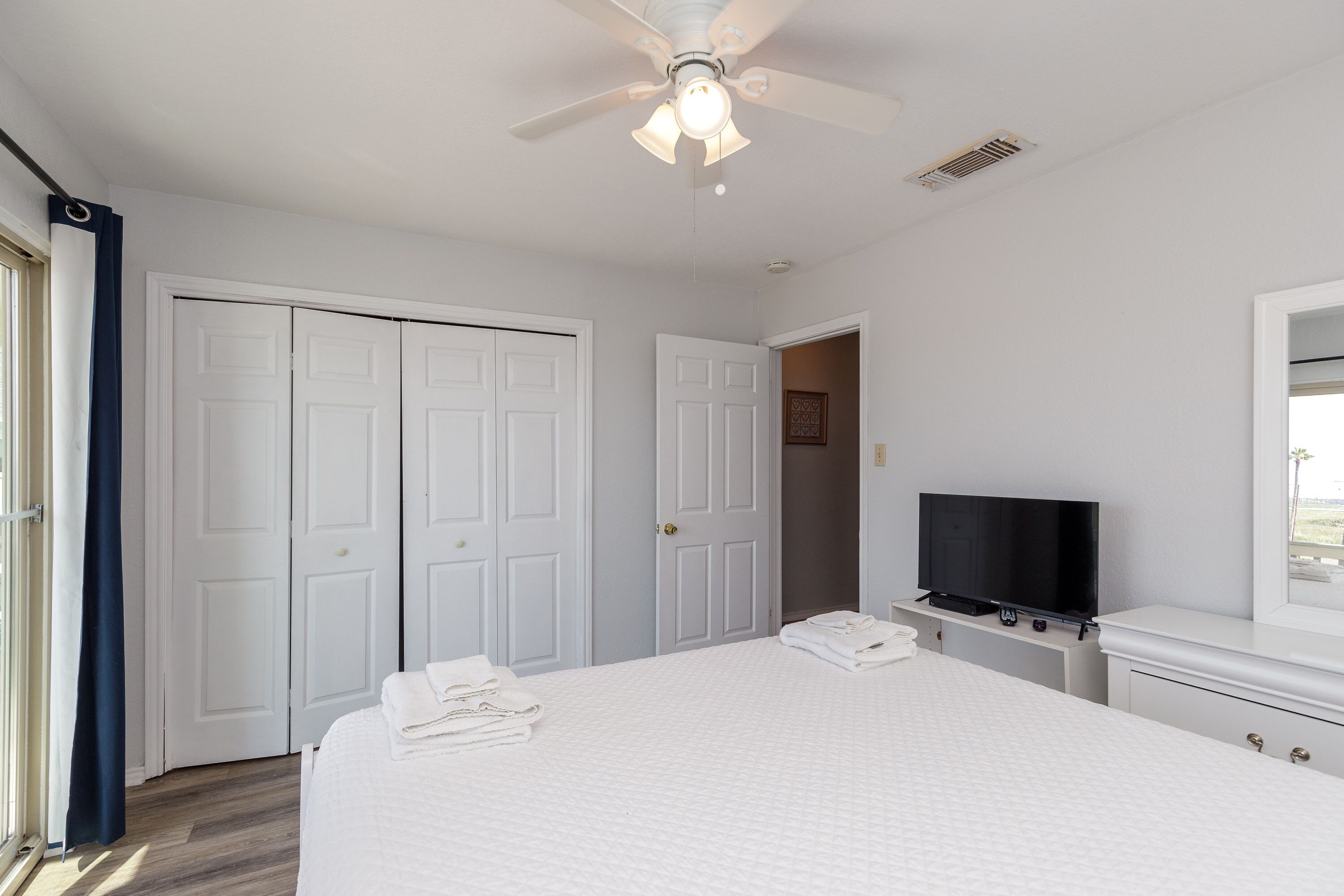 A bedroom with a bed, a ceiling fan, a TV, and a wardrobe.