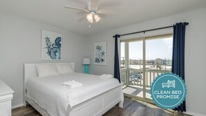 Une chambre à coucher propre et blanche, avec un lit, un ventilateur de plafond et des œuvres d’art accrochées aux murs.