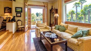 A spacious living room with a wooden floor, a beige sofa, a coffee table, and a view of palm trees through large windows. - Mountain view villa with private pool near Costa Brava (Gerona / Girona)