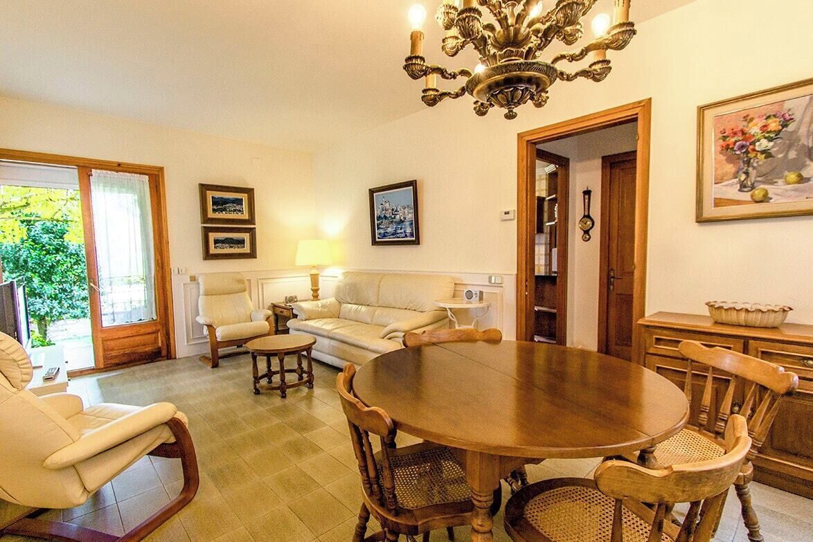 A living room with a round wooden table, two sofas, a chandelier, and a door leading to another room.