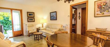 A living room with a round wooden table, two sofas, a chandelier, and a door leading to another room.