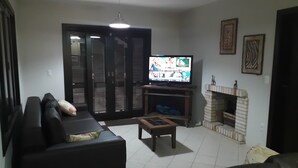 Un salon avec un canapé en cuir noir, un téléviseur, une cheminée et une porte-fenêtre coulissante.