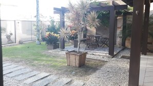 Un patio couvert avec une table et des chaises en bois, entouré de plantes en pot et d’un petit arbre.