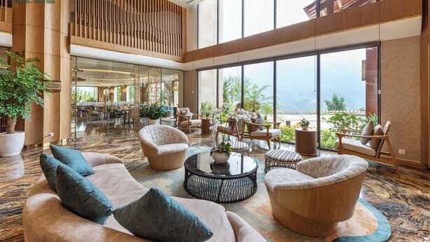 Un vestíbulo amplio con techo alto, ventanas grandes que ofrecen vistas al exterior y diversas opciones de asientos, incluyendo sofás y sillones.