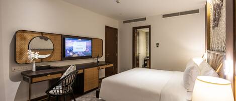 Habitación de hotel con cama, escritorio con computadora, silla, televisor y lámpara.