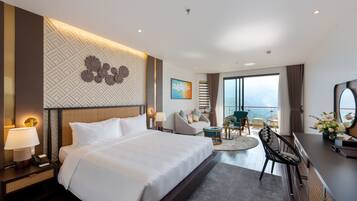 A hotel room with a large bed, a desk with a chair, a small round table, and a balcony with a view.