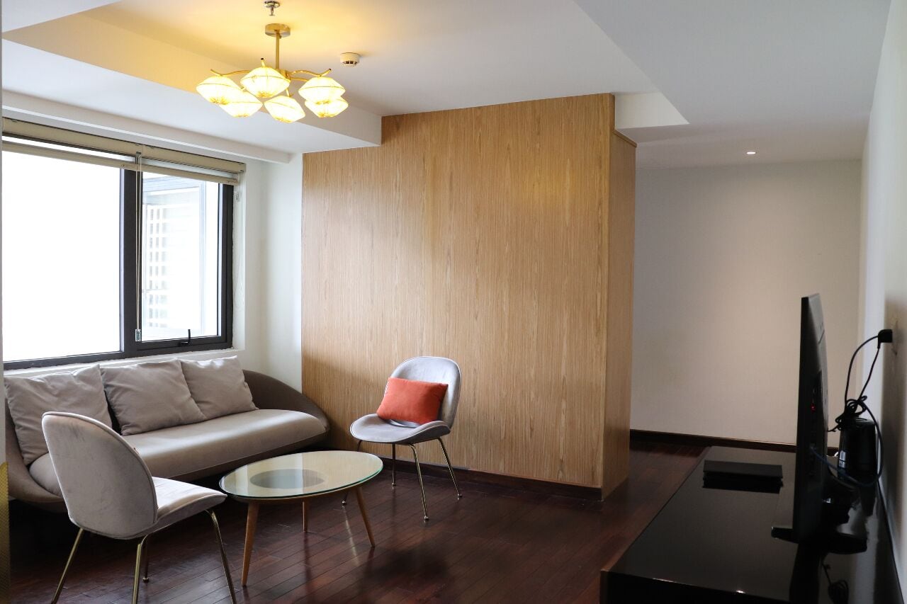 A modern living room with a sofa, two chairs, a small round table, a TV, and a wooden accent wall.