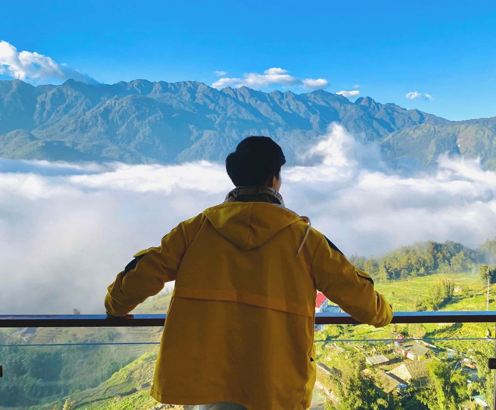 A person in a yellow jacket overlooking a mountainous landscape with a clear sky.