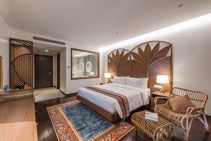 A hotel room with a large bed, a wooden headboard, a nightstand, a wicker chair, and a small table with a magazine.