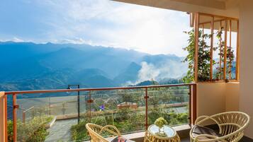 A balcony with wicker chairs, a small table, and a view of mountains and greenery.