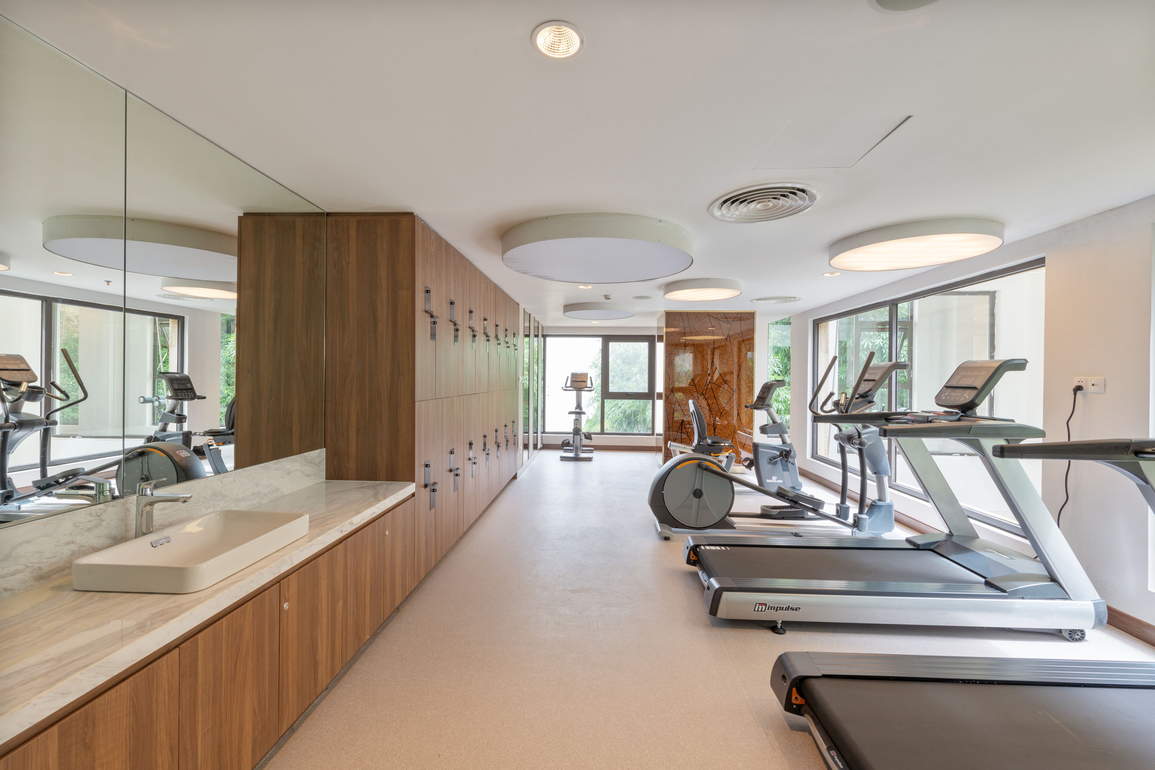 A modern gym with a large mirror, wooden cabinets, a running track, and exercise equipment.