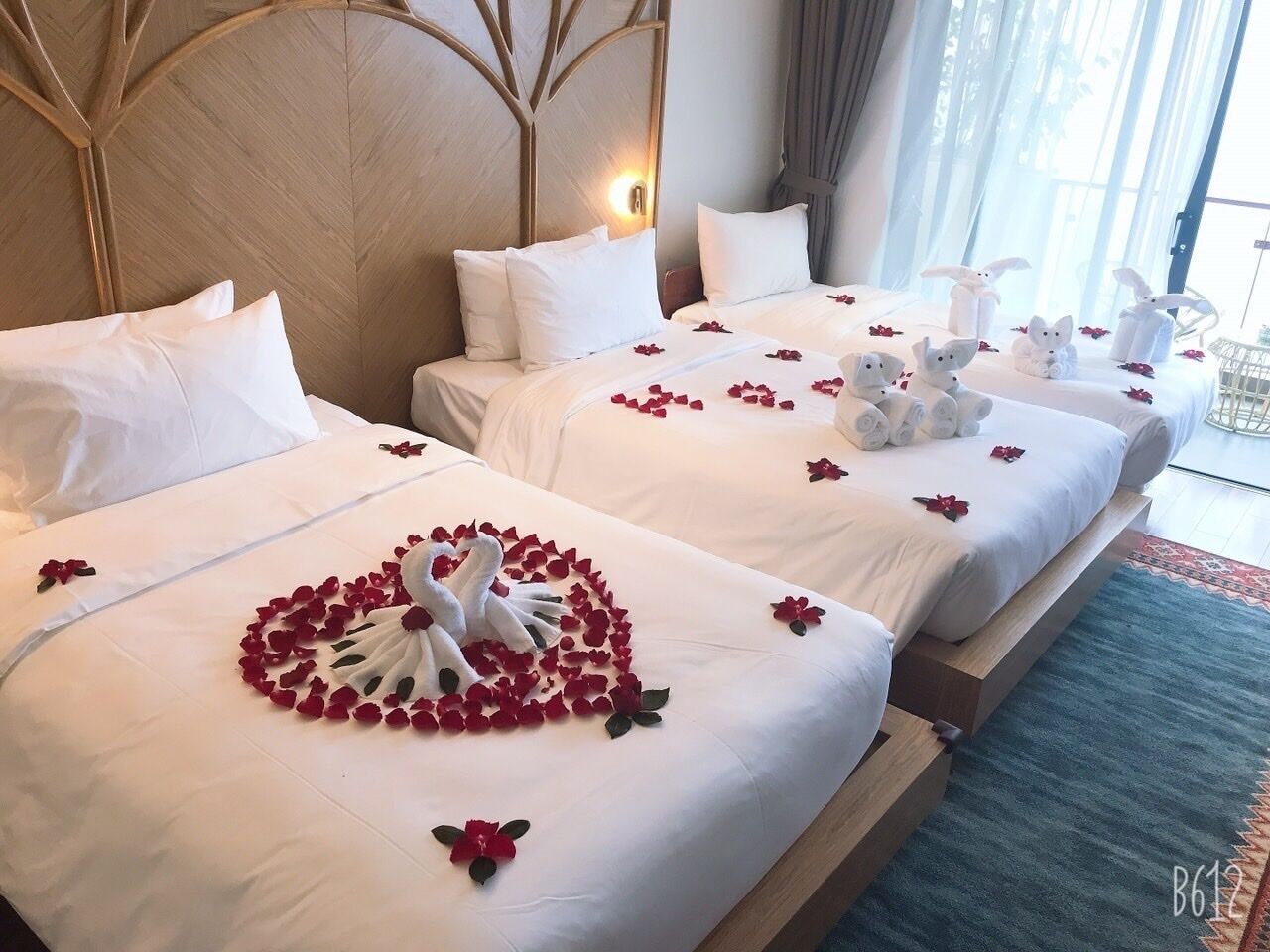 Two hotel beds with white linens, a heart-shaped arrangement of rose petals, and swan-shaped towels.