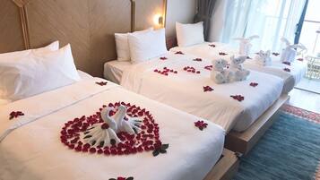 Two hotel beds with white linens, a heart-shaped arrangement of rose petals, and swan-shaped towels.