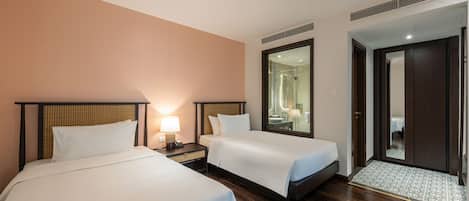 Una habitación de hotel con dos camas, una mesita de noche con lámpara, un espejo grande y suelo de madera.