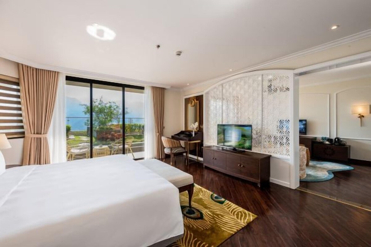 Habitación de hotel con una cama grande, un escritorio con televisor y vistas al exterior.