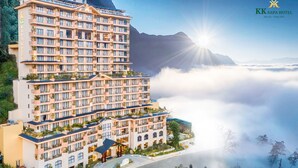 Un hotel de varios pisos con balcones, un jardín en la azotea y vistas a nubes y montañas.