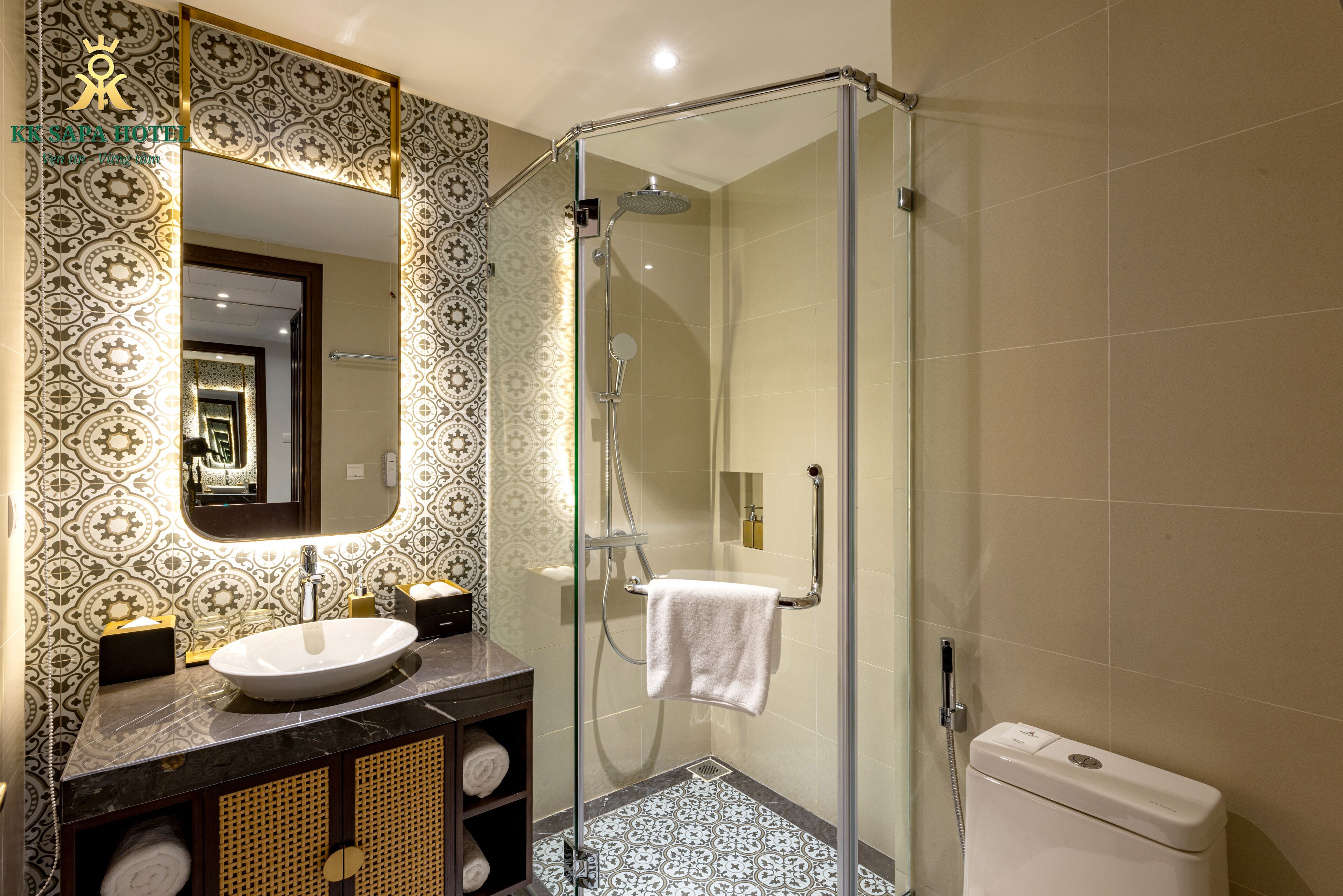 Un baño con ducha de mampara de vidrio, lavamanos con espejo, azulejos con diseño y un inodoro.