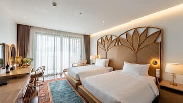 A hotel room with two beds, a wooden headboard, a desk with a chair, a large window with curtains, and a decorative wall panel.