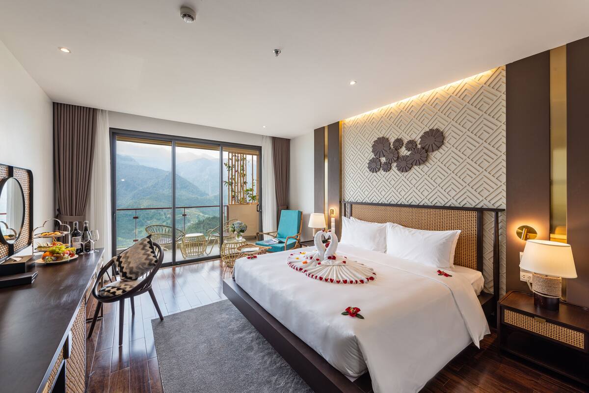 Habitación de hotel con una cama grande, un escritorio con silla, vistas a las montañas y un adorno de pared.