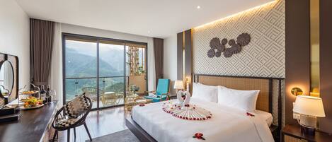 A hotel room with a large bed, a desk with a chair, a view of mountains, and a decorative wall.