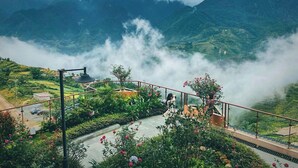 Un balcón con vistas a montañas envueltas en niebla y vegetación exuberante abajo.