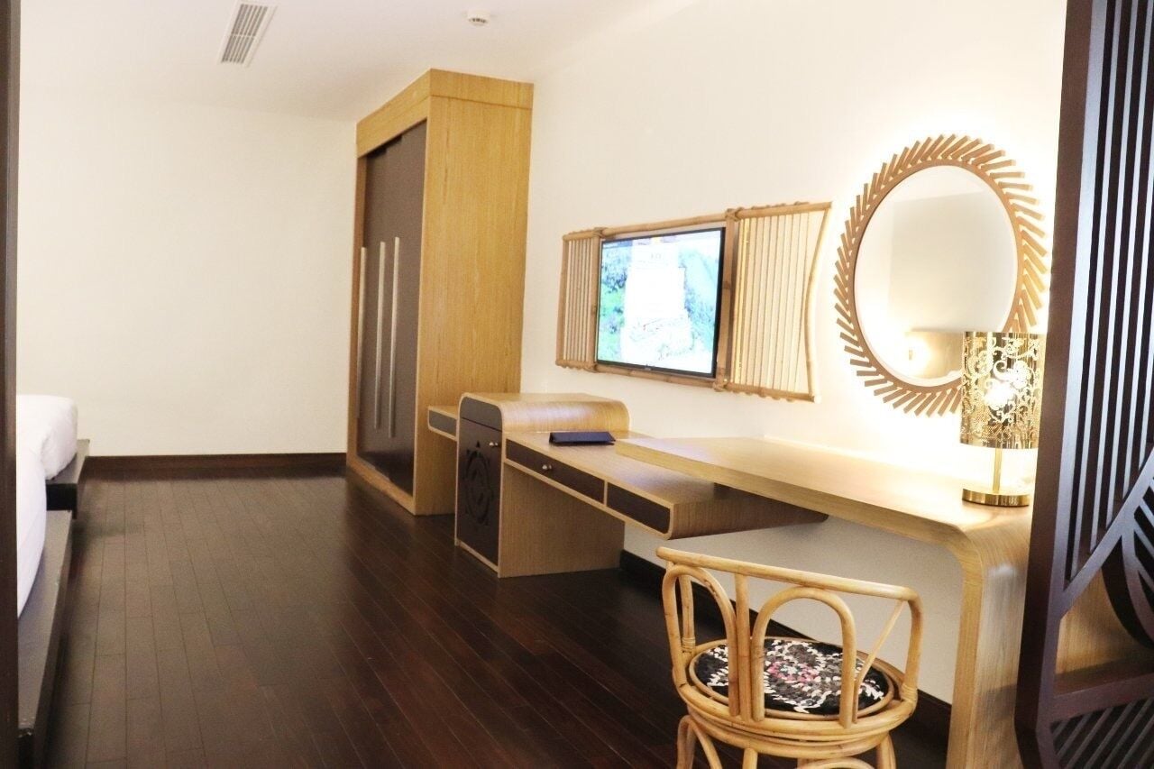 A compact hotel room with a wooden desk, a chair, a bed, a television, and a large mirror.