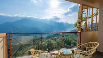 Un balcón con sillas de mimbre y una mesa de vidrio con vistas a un paisaje montañoso.