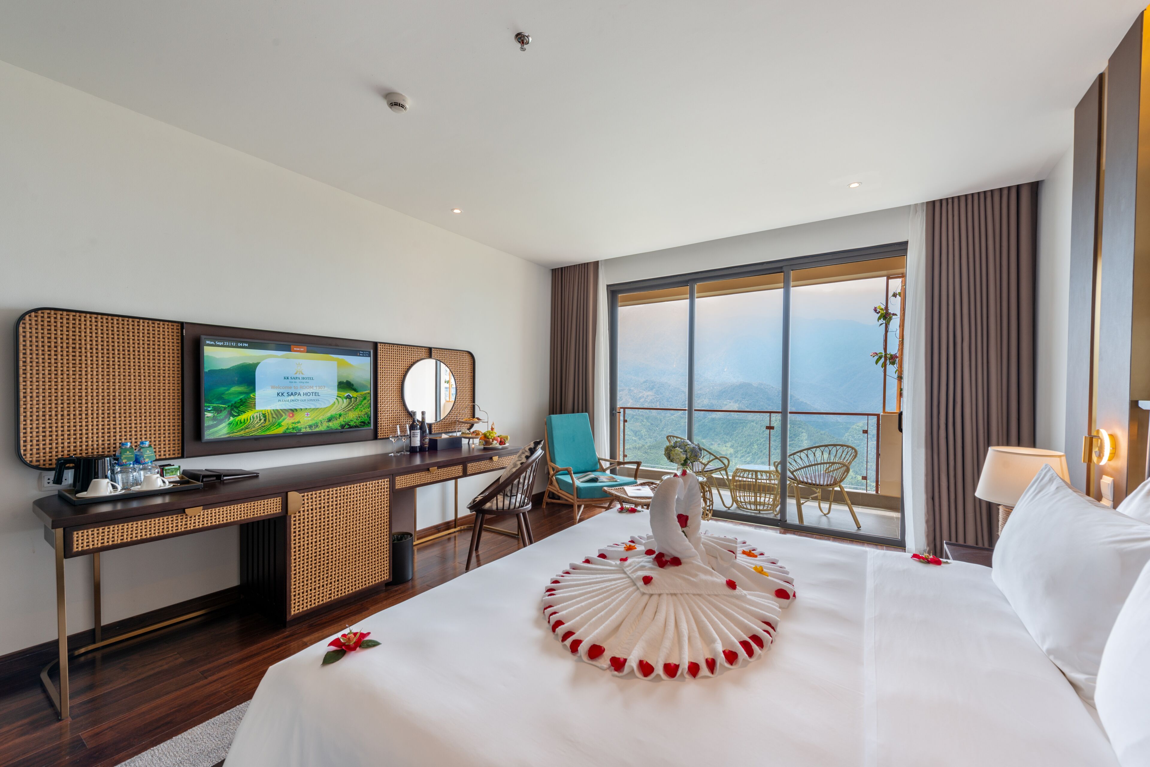 Habitación de hotel con una cama grande, un escritorio con televisor, un balcón con vistas y una decoración de cama en forma de cisne.