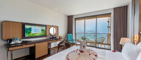 A hotel room with a large bed, a desk with a TV, a balcony with a view, and a swan-shaped bed decoration.
