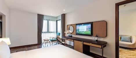 A hotel room with a large bed, a desk with a flat-screen TV, a chair, and a sofa.