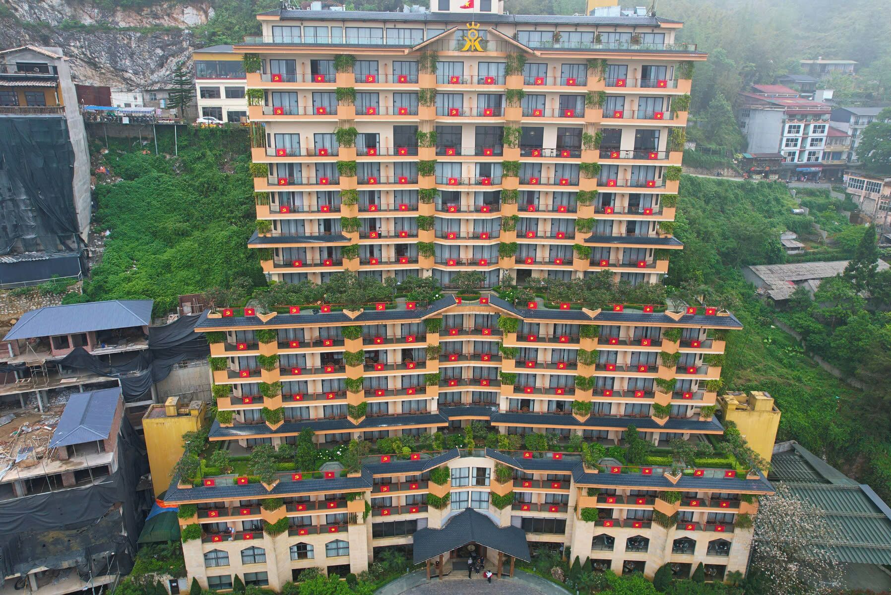 A multi-story hotel with balconies, a central entrance, and surrounding greenery.
