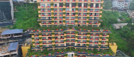 A multi-story hotel with balconies, a central entrance, and surrounding greenery.
