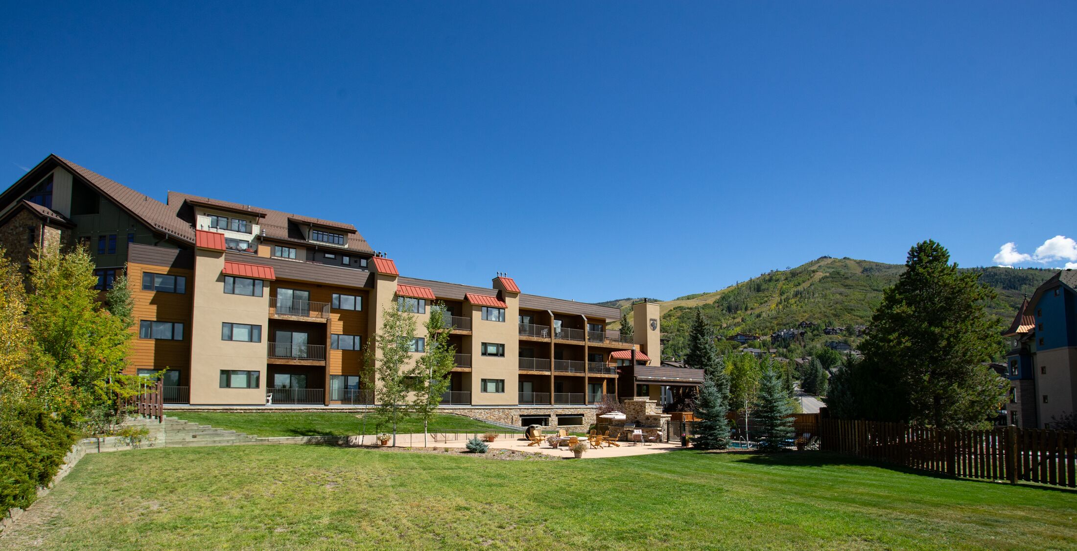 Un hotel de varios pisos con balcones, un patio con asientos al aire libre y montañas al fondo.