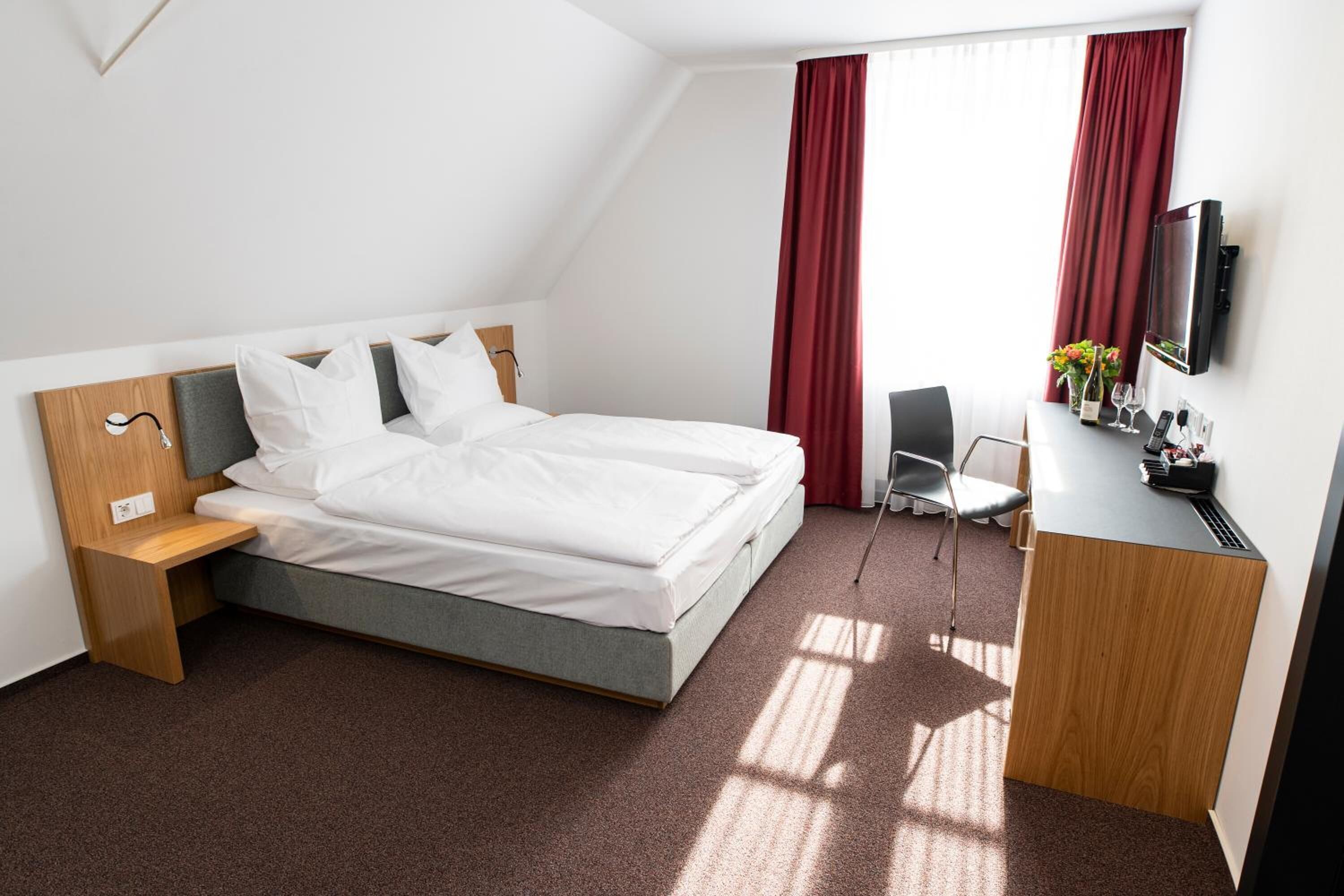 A modern hotel room with a bed, desk, chair, and TV.