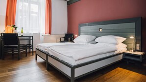 Un dormitorio con cama, mesita de noche, silla y escritorio con lámpara.