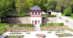 Una piccola torre rossa e bianca con una scala che conduce a una porta, circondata da giardini curati e un muro di pietra.