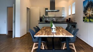 Una cocina moderna con una isla central, un comedor con mesa y sillas de madera, y un cuadro en la pared.