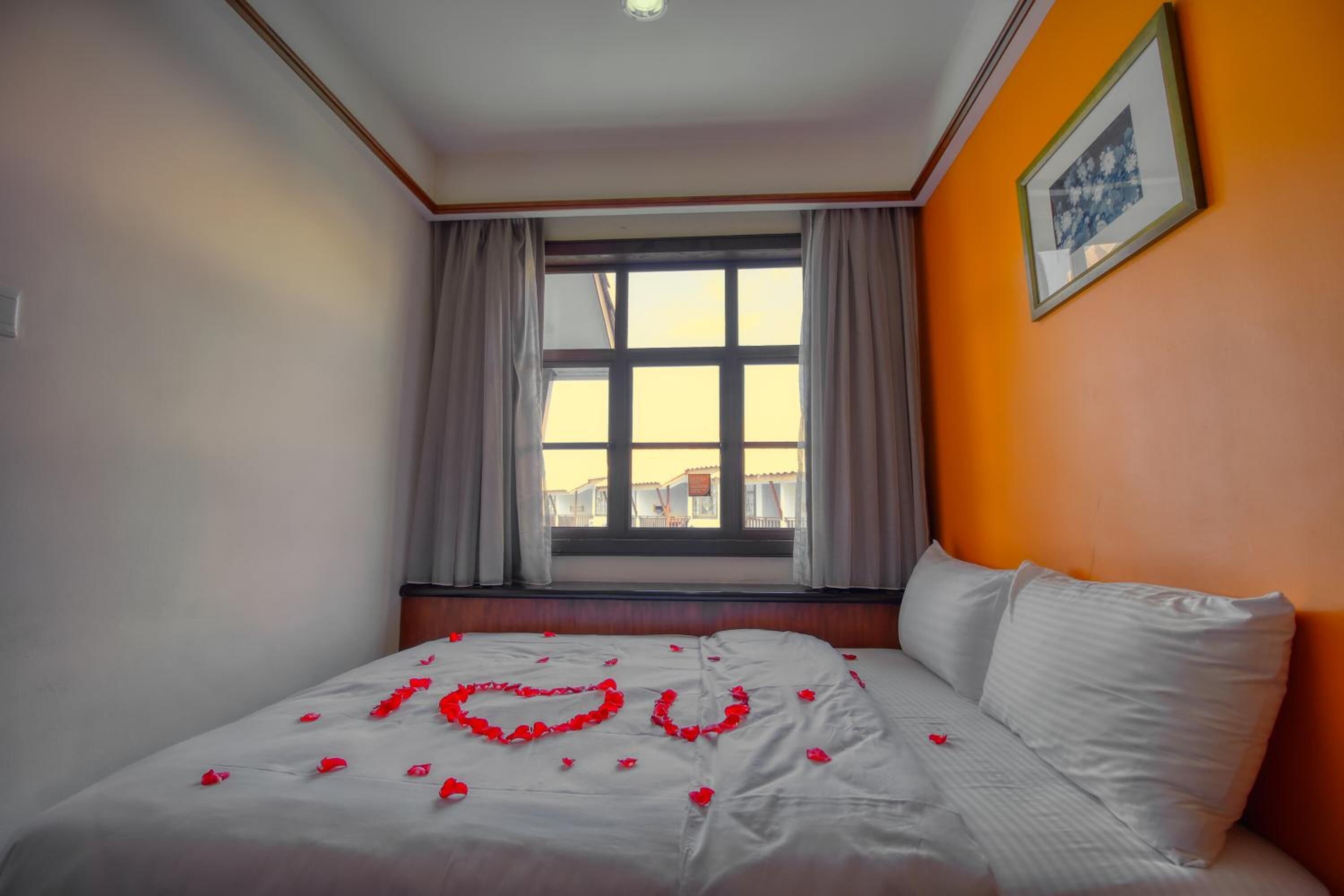A hotel room with a bed, a window with curtains, and a framed picture on the wall.