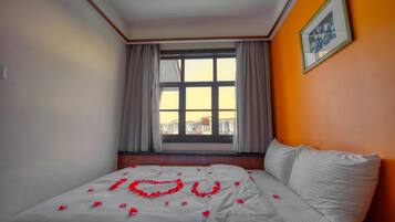 A hotel room with a bed, a window with curtains, and a framed picture on the wall.