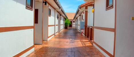 A corridor with tiled flooring, white walls with wooden trim, and a clear blue sky in the background.