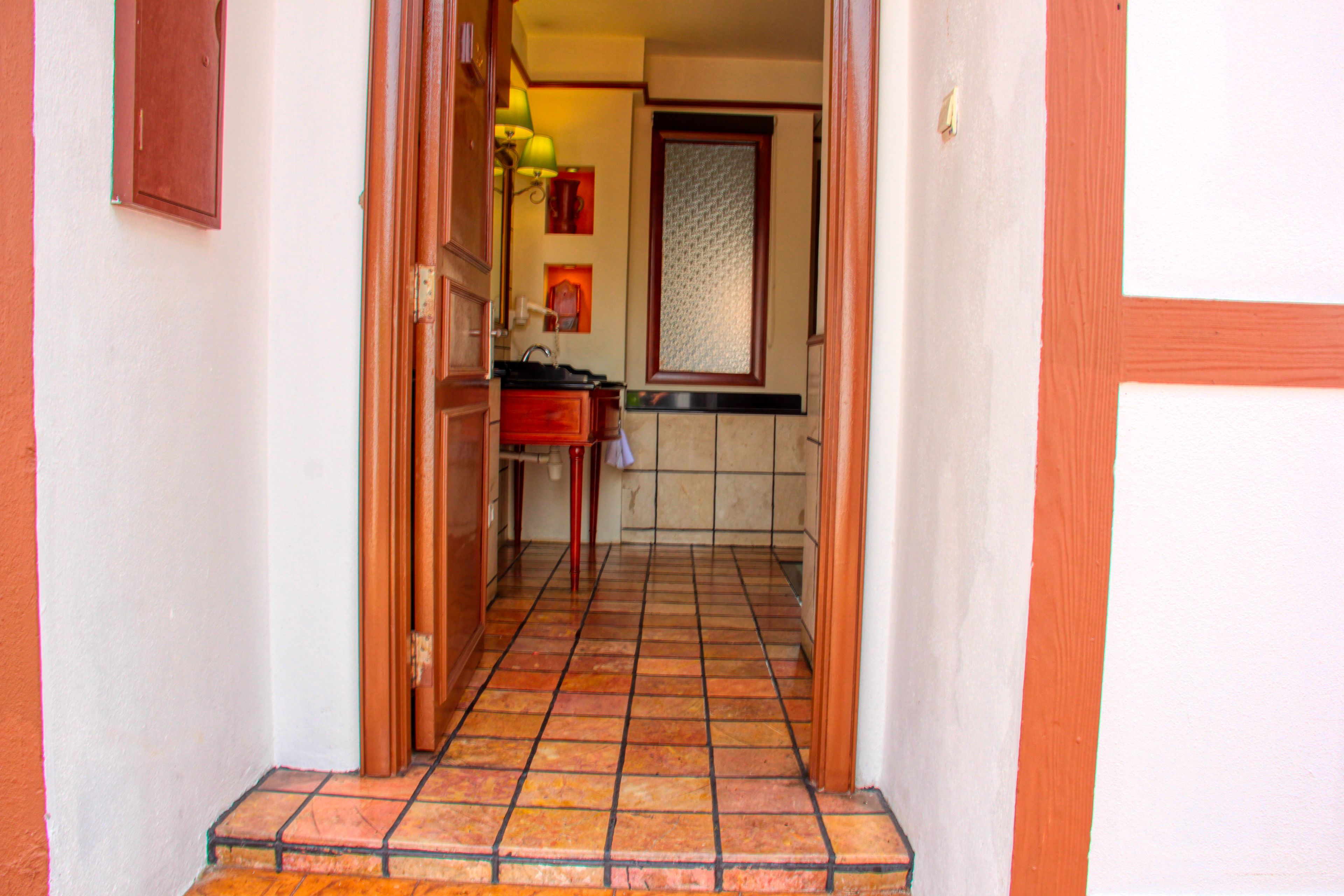 A narrow hallway with a tiled floor, a wooden door, and a small kitchen area with a sink and cabinets.