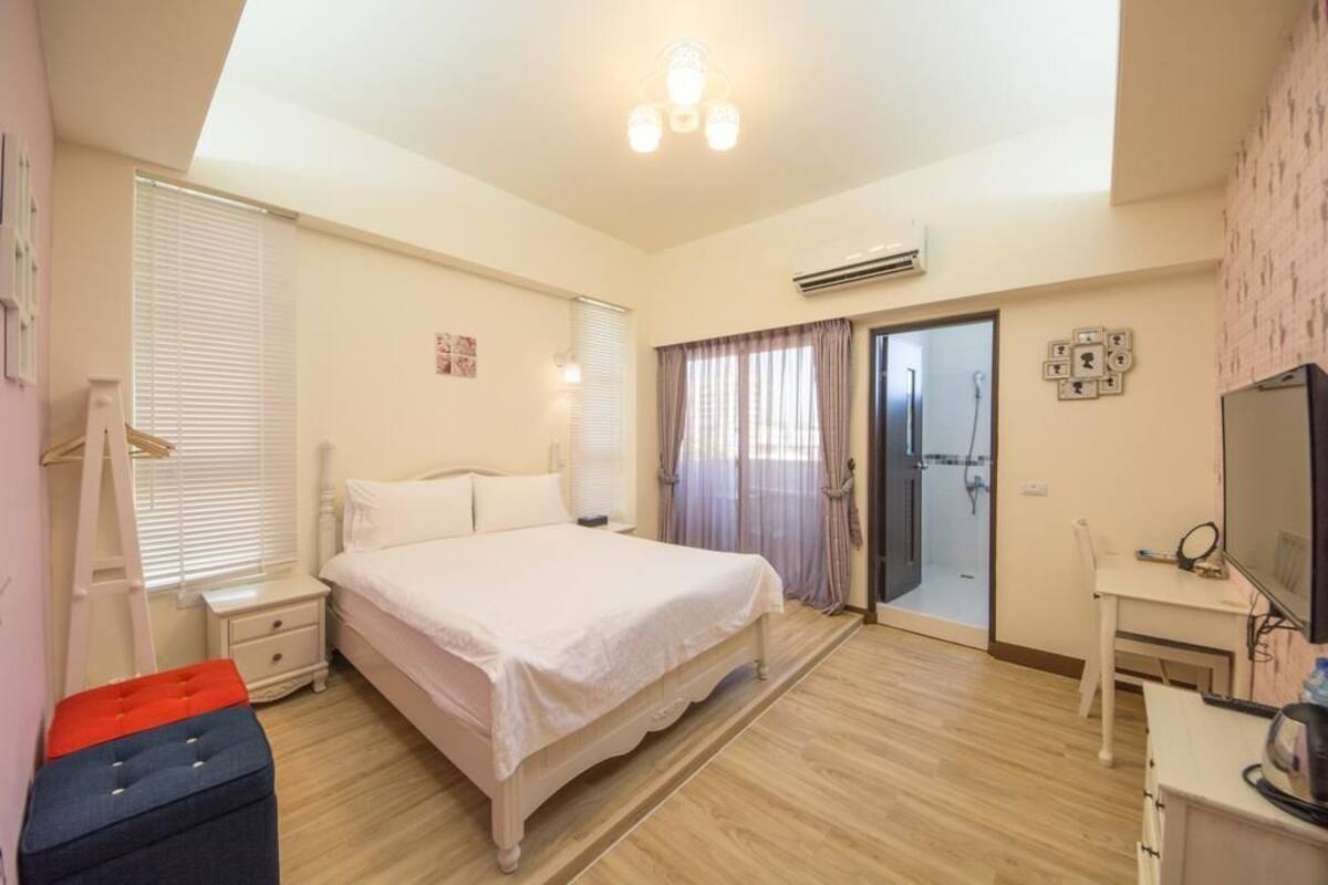 A bedroom with a bed, bedside tables, a desk, a chair, and a television.