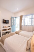 Una habitación con dos camas, un televisor sobre un estante blanco y una puerta azul que da al exterior.