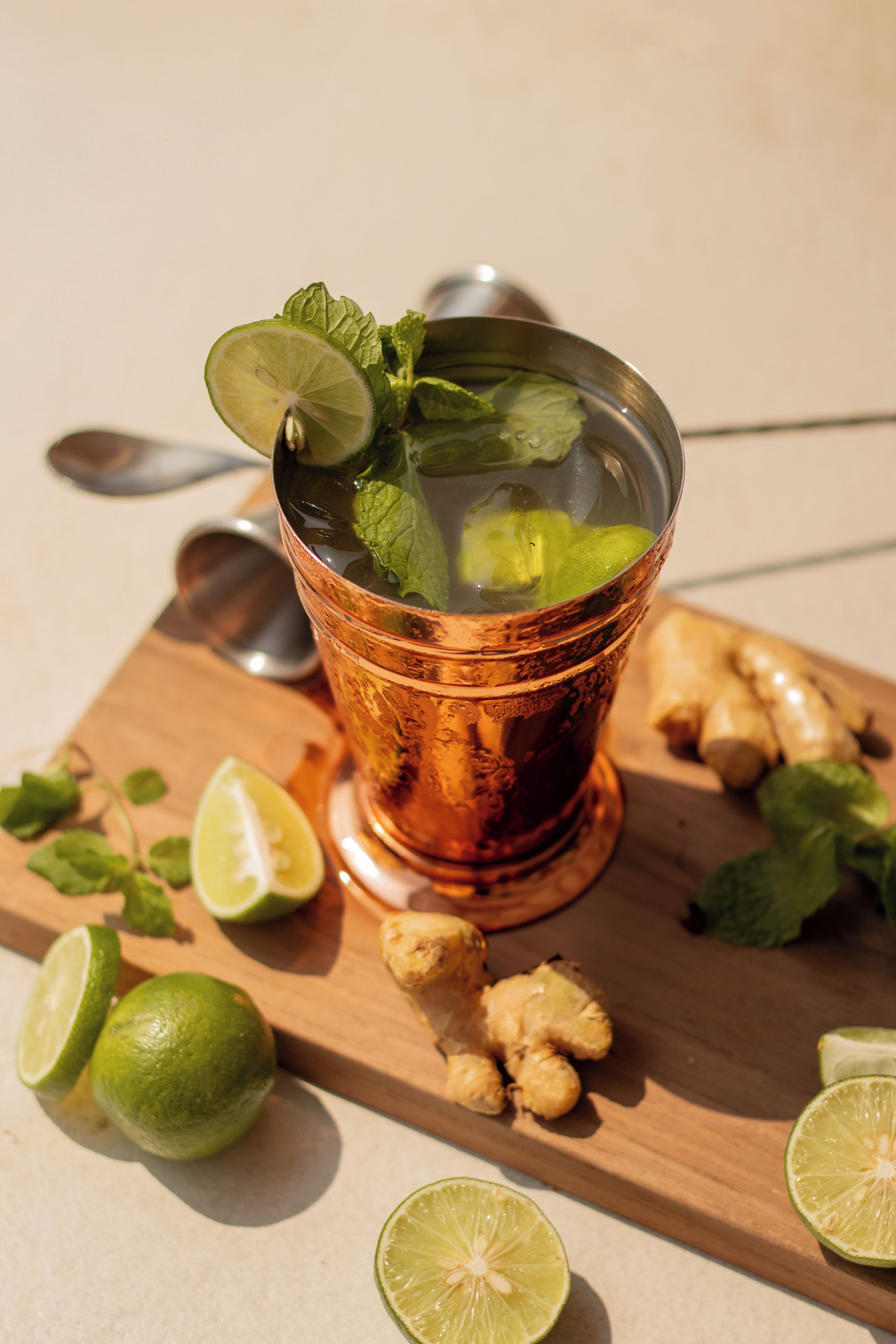 A glass of iced tea with lime and mint on a wooden board with ginger slices and lime halves.