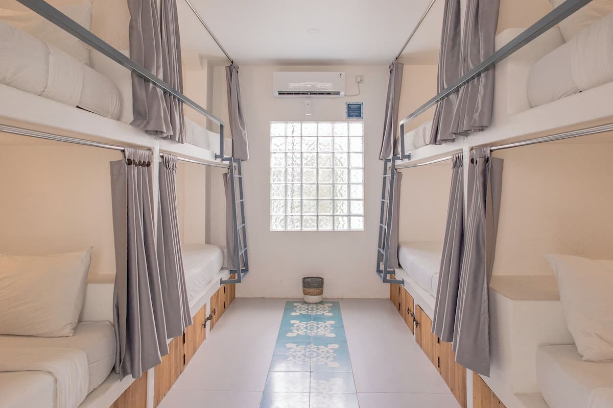 Ein Schlafsaalzimmer mit Etagenbetten, einem Fenster mit Vorhängen und einem blau gemusterten Boden.