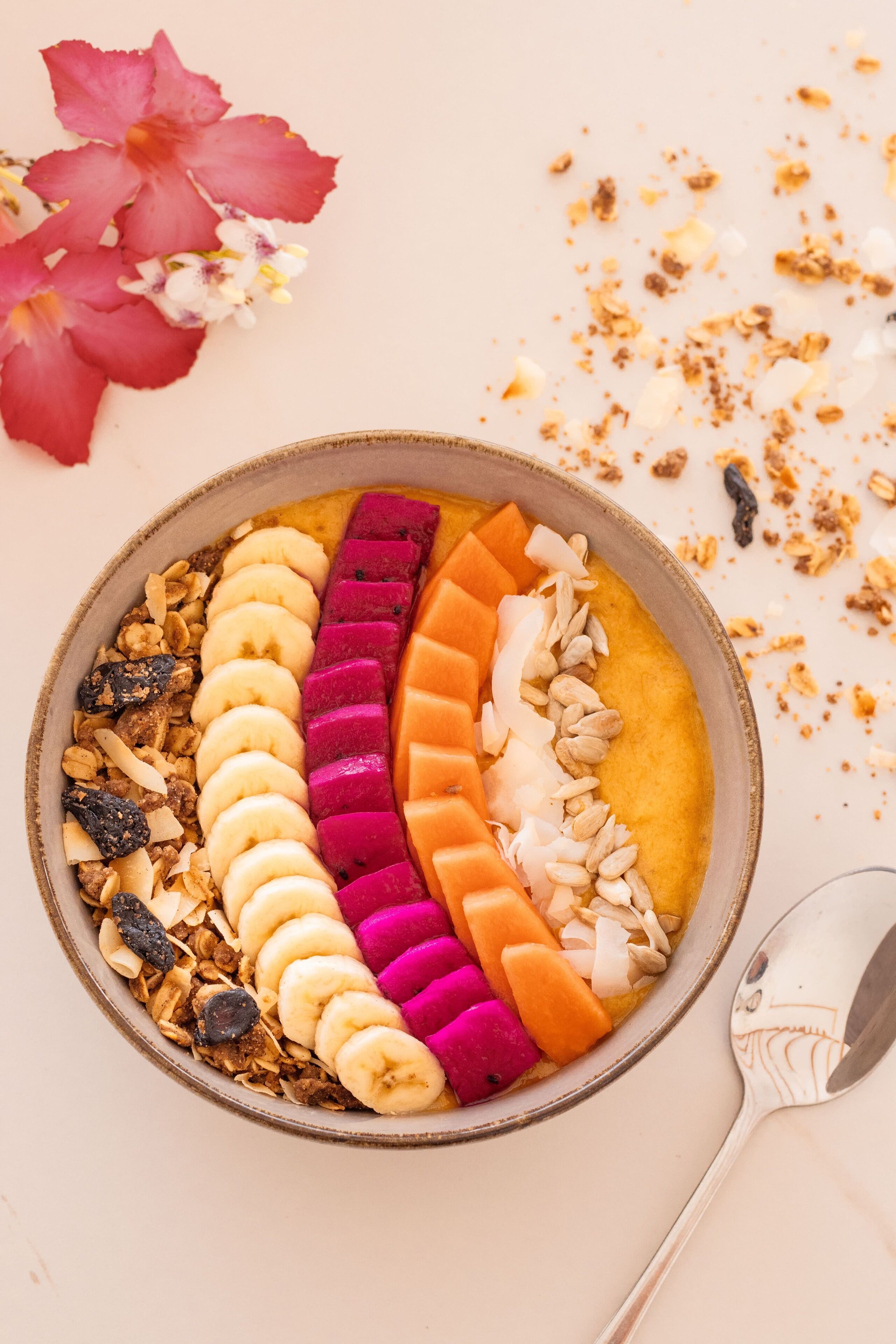 A bowl of colorful fruit and granola on a white surface.